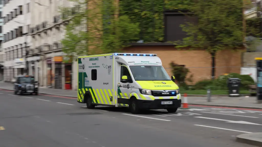 An NHS ambulance driving down a busy city street in London, England.