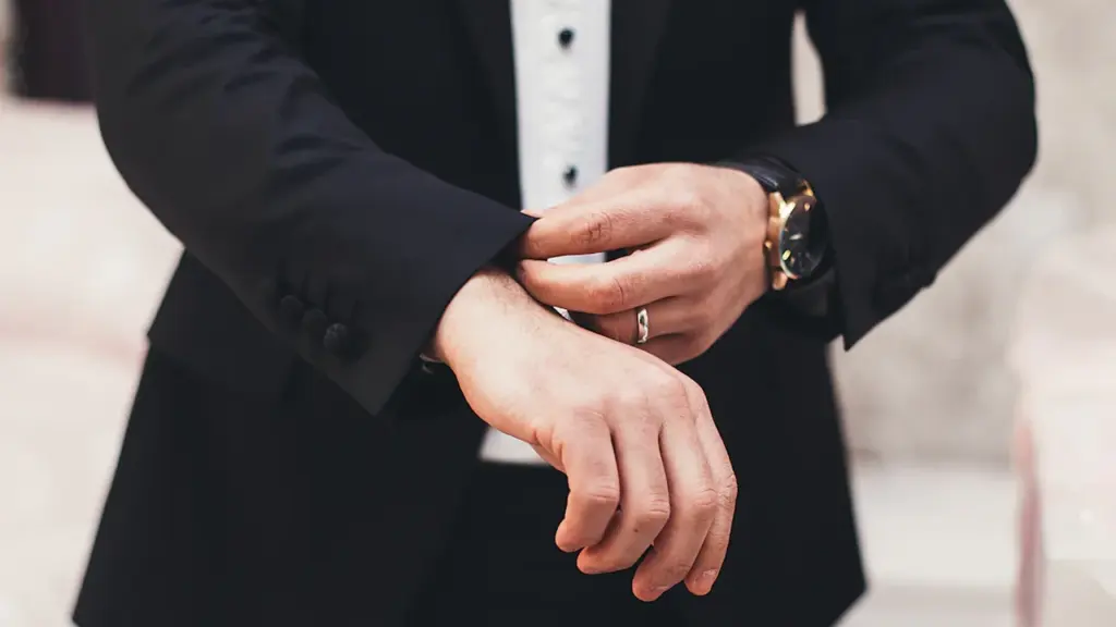A man in a black tuxedo adjusting his cufflinks, evoking classic spy style.