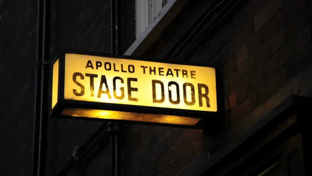 Illuminated yellow Apollo Theatre stage door sign attached to a brick wall