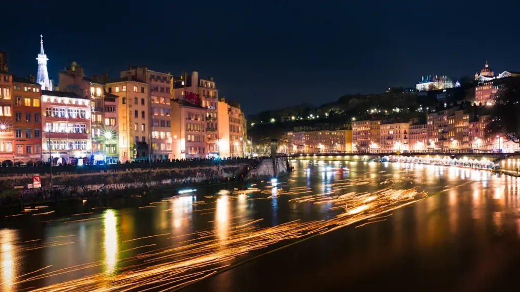 Evening view of historic European riverfront buildings with lights reflecting on the water.