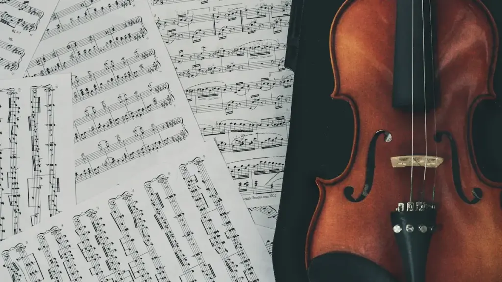 Classic wooden violin resting beside scattered sheets of musical notation scores