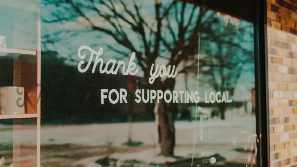 A shop window sign reading Thank you for supporting local on a city street.
