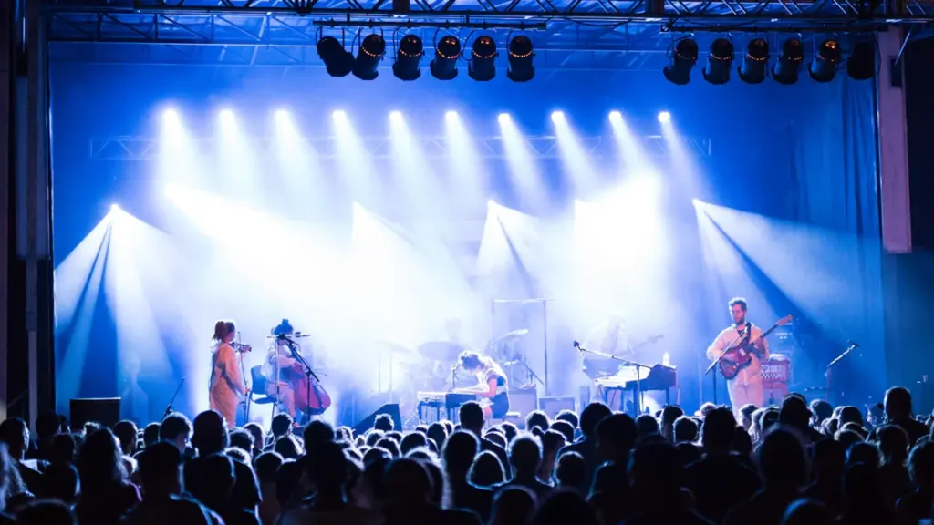 Silhouetted crowd watching a live band perform on a brightly lit concert stage.