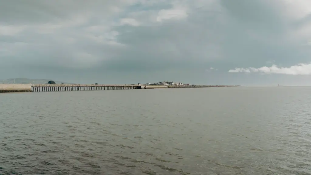 A distant pier extending into calm ocean water near a coastal town.