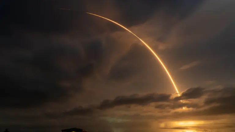 SpaceX Falcon 9 rocket launching into the night sky over a cloudy horizon.