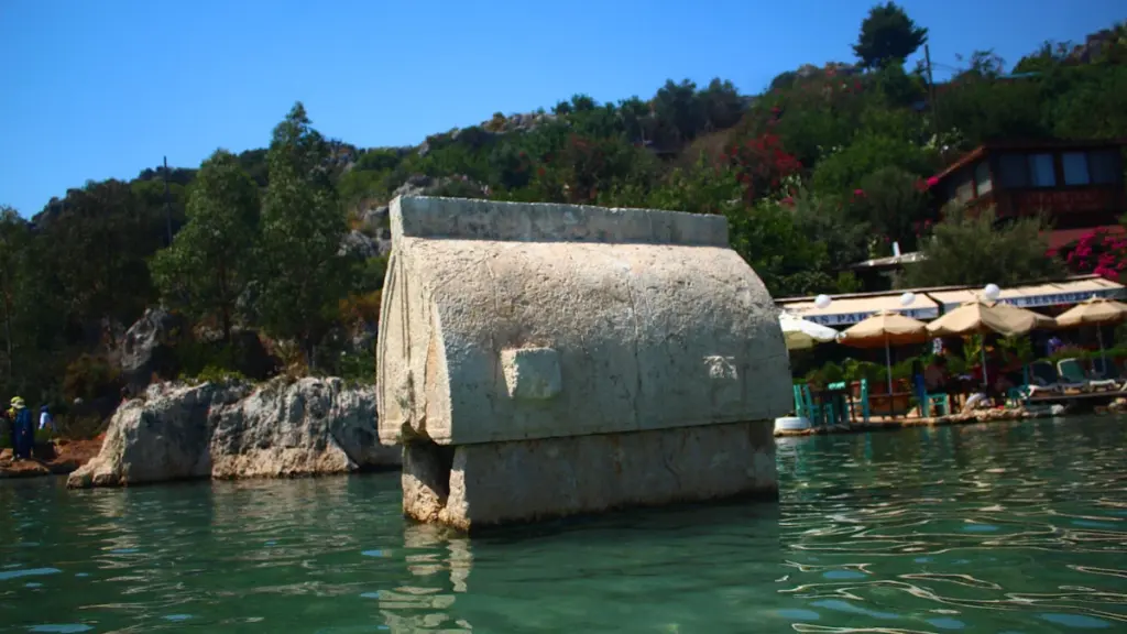 An ancient stone tomb partially submerged in clear, bright turquoise coastal water.