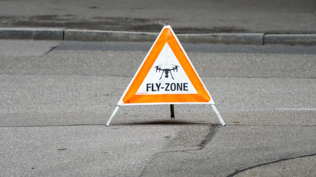 A triangular yellow street sign warning of a drone fly zone area.