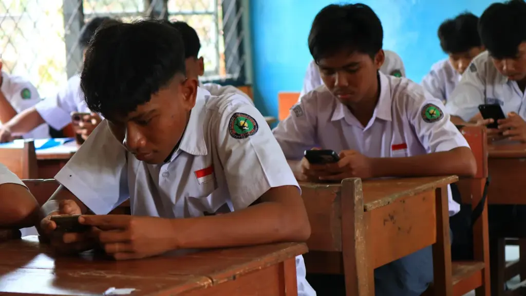 Students in a classroom setting focusing on their smartphone screens during a lesson.