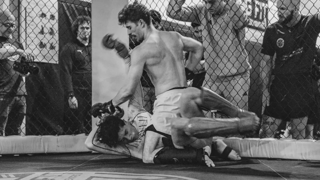 Two mixed martial arts fighters grappling intensely inside a training cage in Manchester.